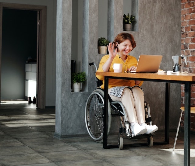 woman on a wheelchair working on a laptop which s on the table